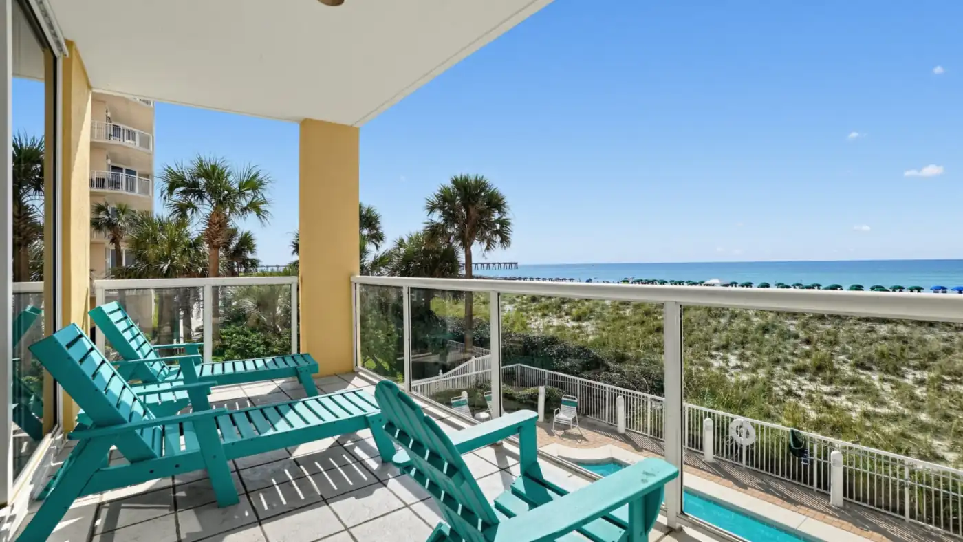 Condo balcony with teal Adirondack chairs overlooking the dunes, a pool and the Gulf of Mexico on Navarre Beach